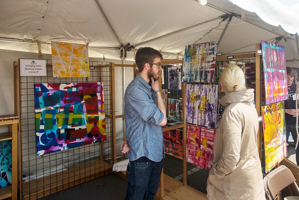 <p>Lansing resident Matthew Holben shares his art with a customer on May 18, 2014, on Albert St., in front of Hopcat. The festival allowed various artists to display many different types of artwork and consumer goods. Hayden Fennoy/The State News</p>