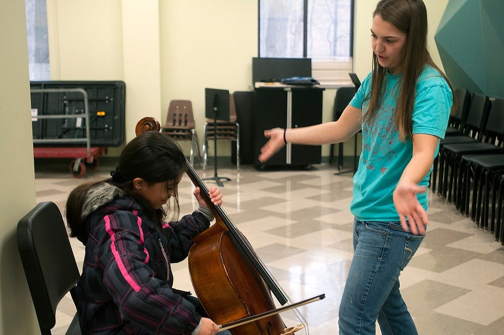 <p>Vocal performance senior and Community Music School intern Katharine Nunn shows East Lansing resident Aljadel Assaf how to play the cello Jan. 17, 2015, at the MSU Community Music School open house, 4930 South Hagadorn Rd. in East Lansing. Assaf was trying out the cello because she recently received a guitar and figures the instruments are somewhat similar. Allyson Telgenhof/The State News.</p>