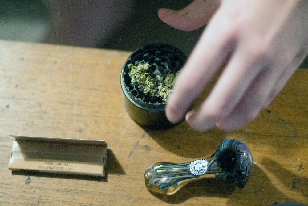 <p>An anonymous student grinds down marijuana in preparation to smoke it. Nearby, a pipe and smoking papers.</p>
