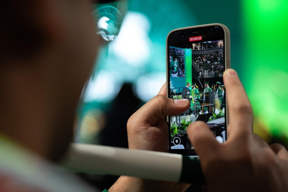 A graduate records their friend from a phone during commencements at the Breslin Center on May 3, 2025.