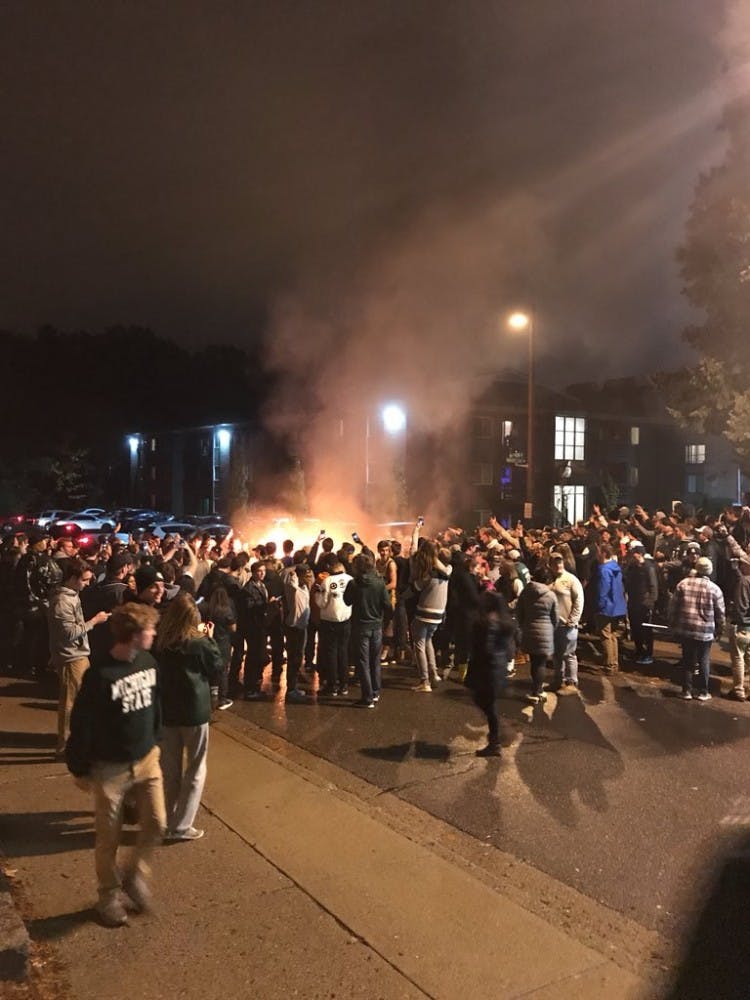 Dozens gather around furniture set on fire to celebrate MSU's win over Penn State. Officials extinguished the fire by approximately 7:40 p.m.