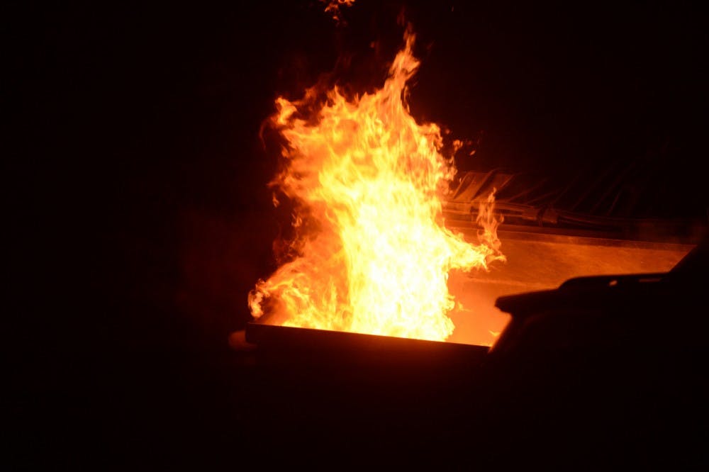 A dumpster fire burns on Dec. 5, 2015 in Cedar Village. Hundreds of students gathered in the streets of Cedar Village to celebrate MSU's victory over Iowa in the Big Ten championship, resulting in police action. 