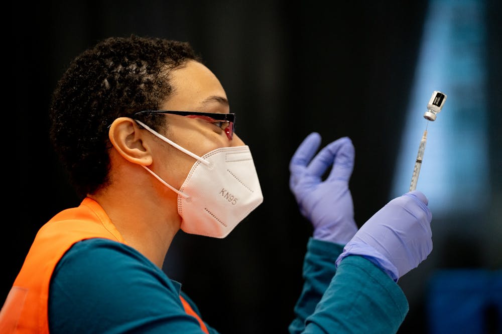 <p>Kamaya Young fills vaccine syringes, sorting them by vaccine, during the COVID-19 vaccine booster clinic at the Breslin Center on Jan. 26, 2022.</p>