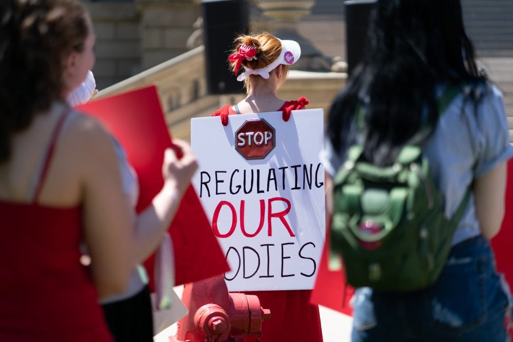 <p>Abortion Ban Protest at Michigan State Capitol on June 22. Protest attendee wears a red robe and white hat.</p>