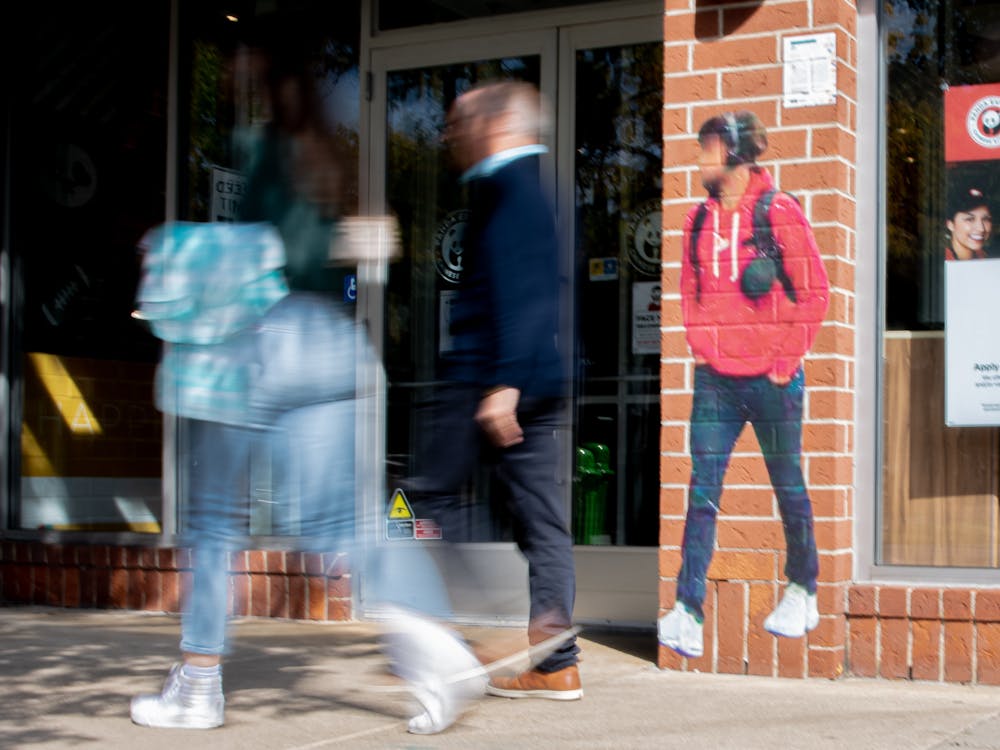 Two people walk past one of artist Paolo Cirio's "Street Ghost" on Sept. 30, 2021. "Street Ghosts" are scattered around East Lansing, depicting blurred images of people Cirio found on google maps, and is a part of the Michigan State University Museum's Tracked and Traced exhibit.