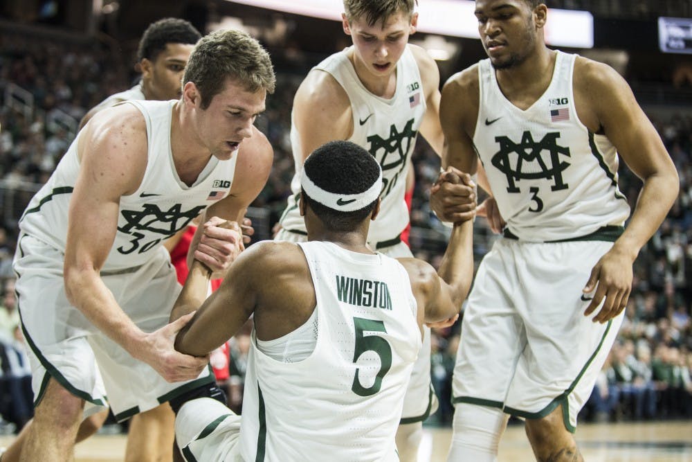 Senior guard Alvin Ellis III (3), right, and teammates help freshman guard Cassius Winston (5) up off of the court floor during the second half of the men's basketball game against Ohio State University on Feb. 14, 2017 at Breslin Center. The Spartans defeated the Buckeyes, 74-66.