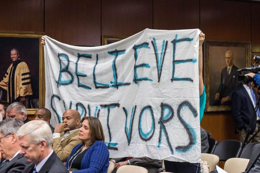 Members of Reclaim MSU hold up signs of protest at the Board of Trustees meeting on Oct. 26, 2018.