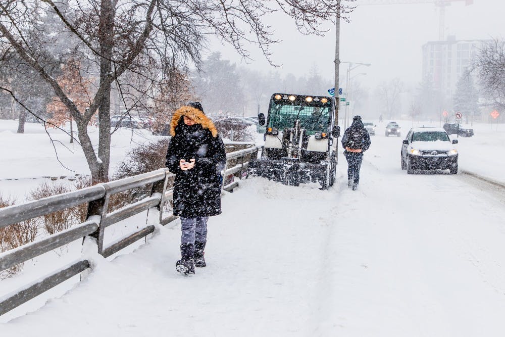 <p>Students move out of the way of the snow plow while crossing the bridge on Bogue Street on Jan. 28, 2019, at Michigan State University.</p>