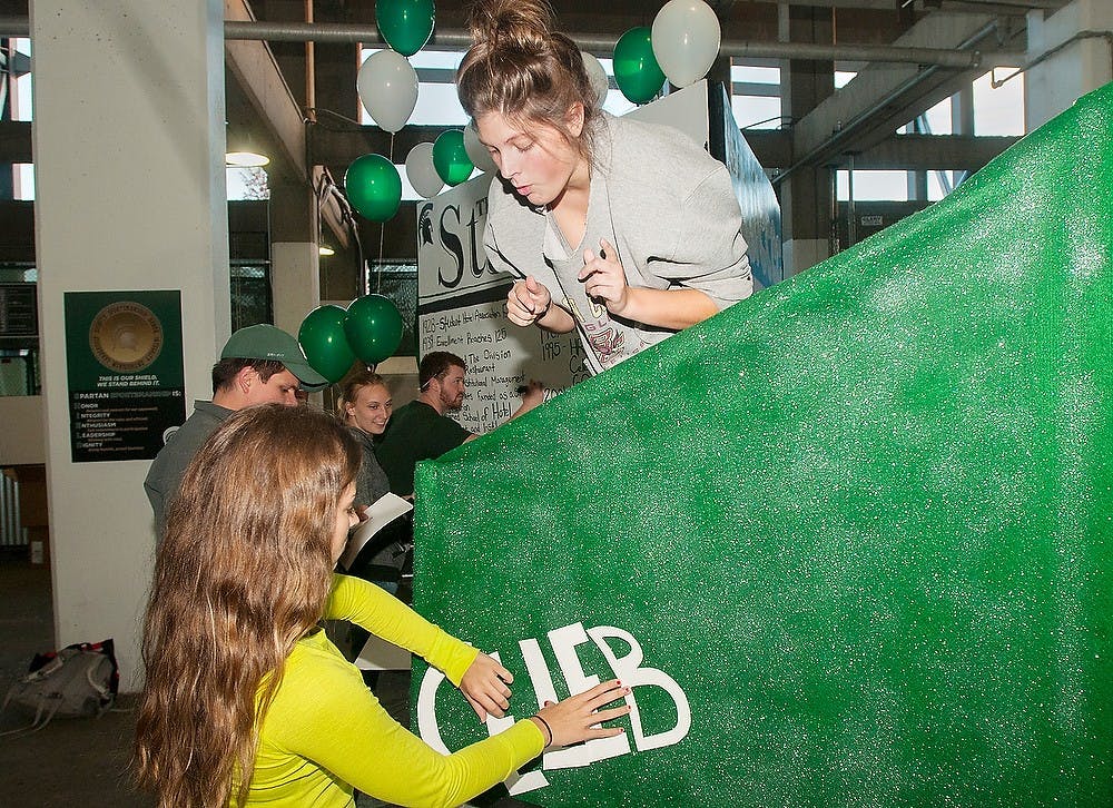 <p>Hospitality business seniors Taylor Pahl, left, and Jessica Dupont work on their float for the School of Hospitality Business on Sept. 24, 2014, at Spartan Stadium. The float will be seen at the MSU Homecoming Parade on Friday. This year's parade float theme is Spartans make headlines.  Raymond Williams/The State News</p>