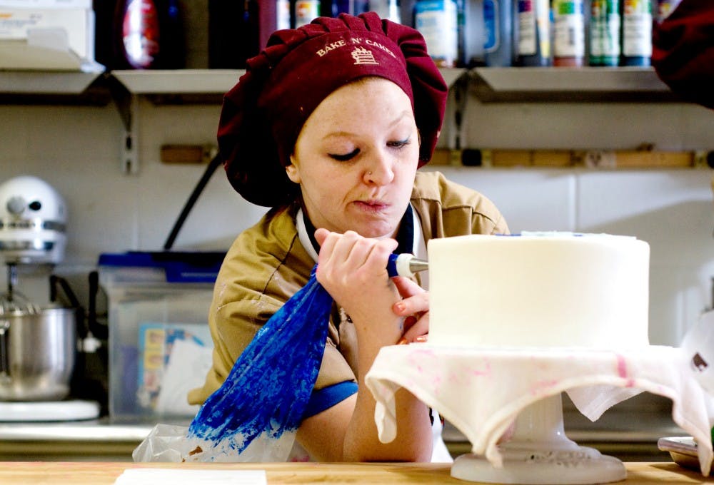 Colette Moore, a cake decorator, designs a cake at Bake N' Cakes, 3003 E. Kalamazoo St., on March 3. Moore, while in her first year at vocational school at Oakland Technical Campus, was given an assistant position in the bakery because her teacher noticed her handwriting skills. Moore said she has always been artistic, and grew up in a body shop where she watched the artists air brush designs onto the cars.  Lauren Wood/The State News