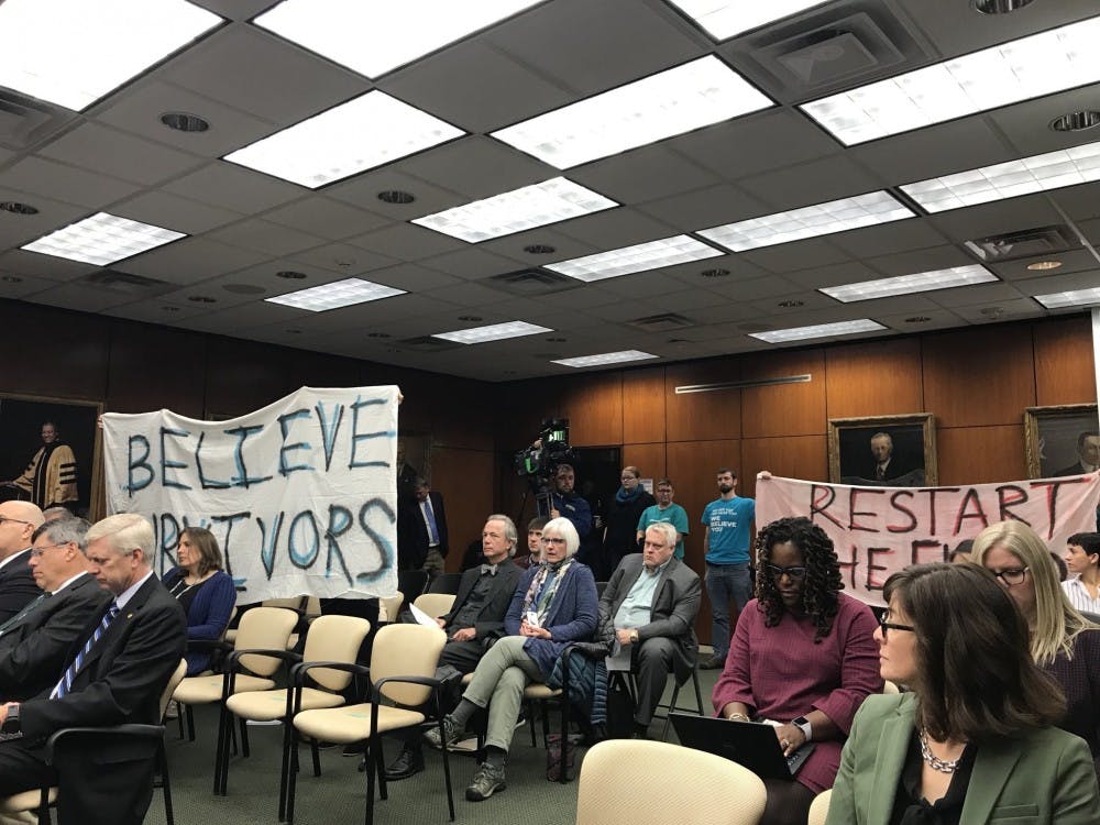 <p>Members of the MSU community hold up signs during the Board of Trustees meeting on Oct. 26, 2018.&nbsp;</p>