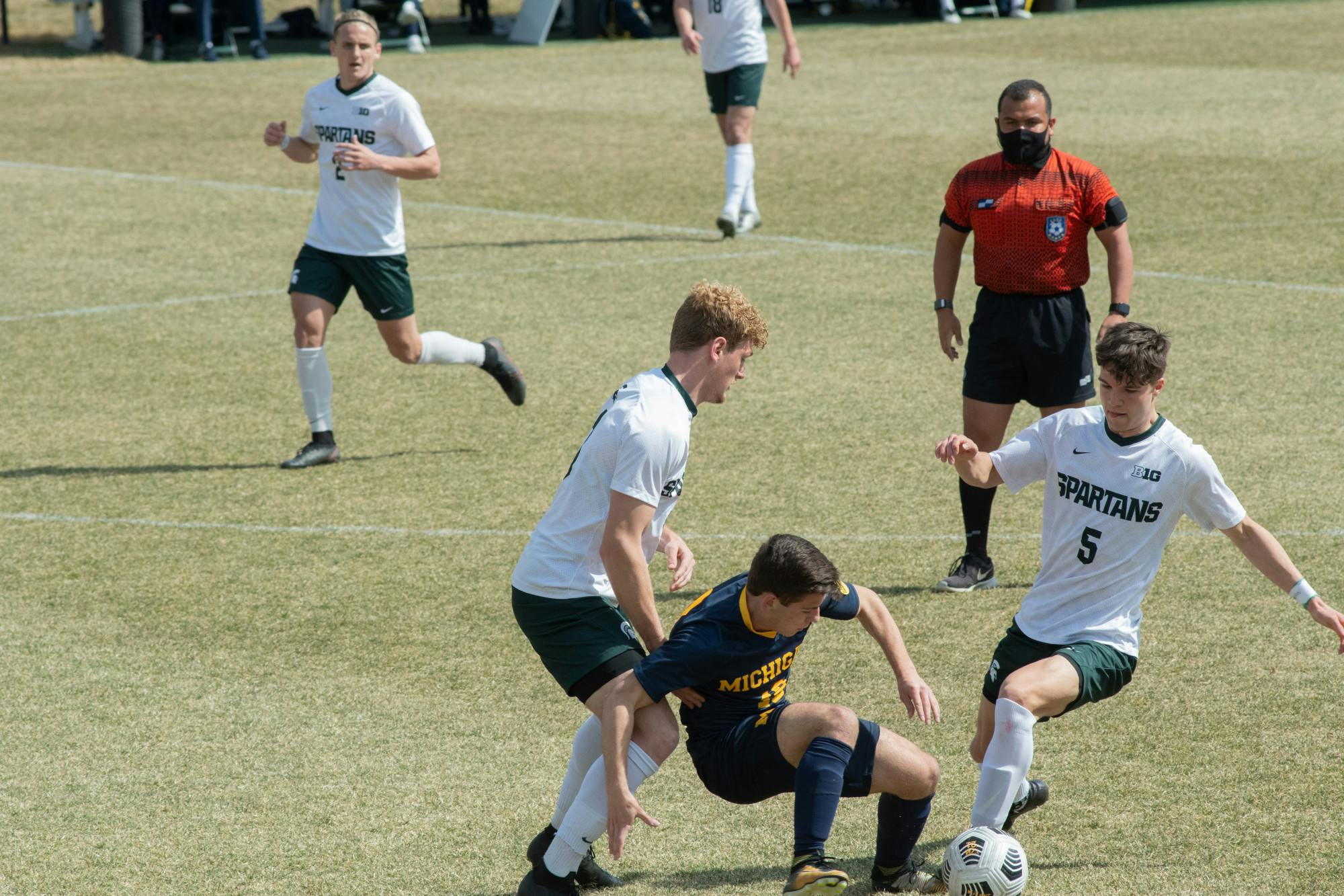 University of Michigan's Jacob Nunner (18) falls as Michigan State's Jack Zugay (5) attempts to retrieve the ball in the Spartans' loss on March 23, 2021.