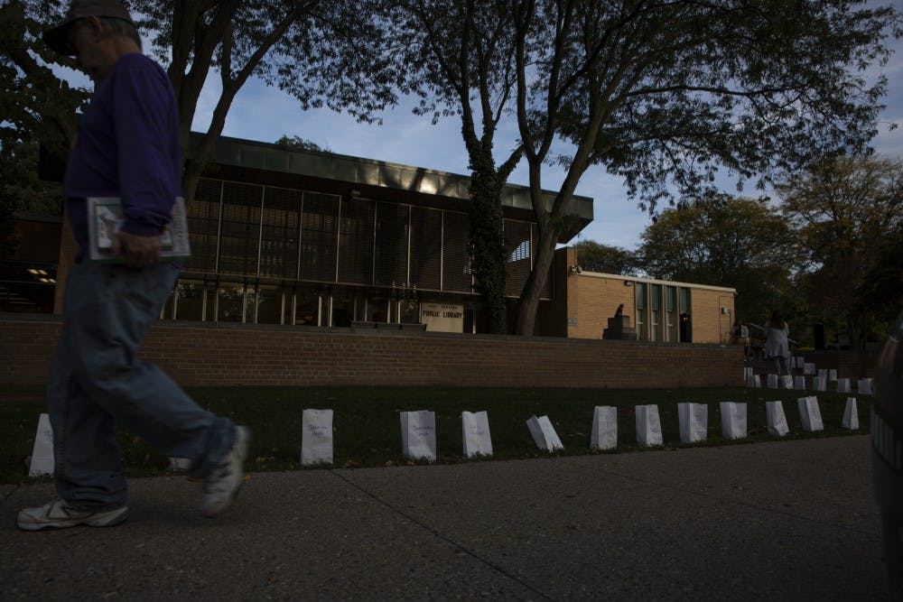 A man walks by rows of luminaries on Oct. 10, 2019 at the East Lansing Public Library. POSSE lit 505 luminaries signifying the known survivors Larry Nassar at the East Lansing Public Library, before President Stanley’s meeting with survivors. 