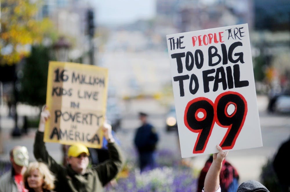 Demonstrators holding signs at the Occupy Lansing protest Saturday afternoon in front of the state Capitol. The demonstration featured a variety of agendas, from stronger support to Medicare, less dependent on foreign manufacturing goods, to call for the end of the Federal Reserve System. Justin Wan/The State News