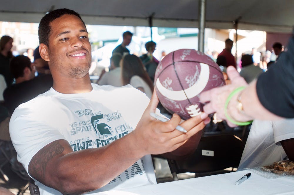 Junior defensive end, William Gholston signs a football for a Spartan fan Tuesday, Aug. 14, 2012 in downtown East Lansing. The event, titled Meet the Spartans drew thousands of MSU football fans downtown. Adam Toolin/The State News