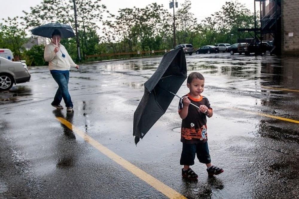 <p>East Lansing resident Sema’J Benson, 2, walks with umbrella in hand with his mother Judy Torp behind him, Tuesday, May 28, 2013, in Lansing. Justin Wan/The State News</p>