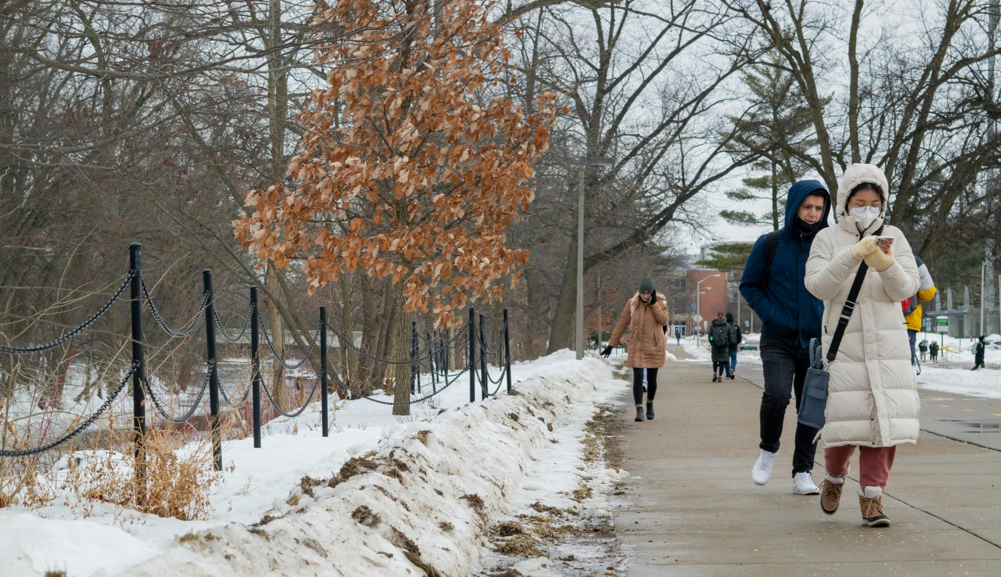 Students are oblivious as they walk by the temporary fence on Red Cedar road. The fence was put up as a result of the loss of Grand Valley student Brendan Santo. Shot on Feb 10, 2022