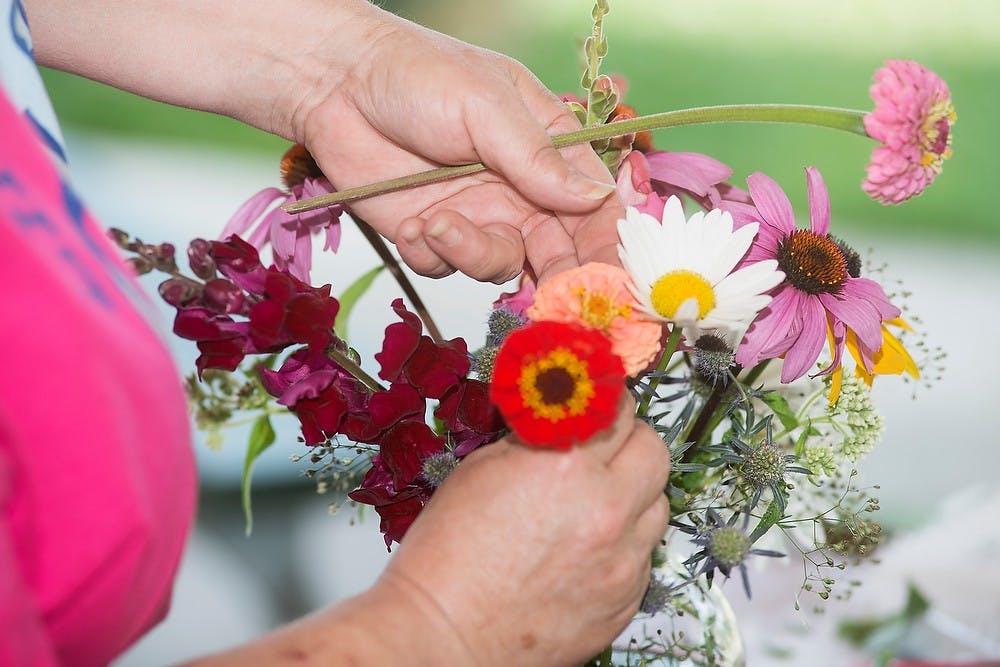 <p>Williamston, Mich., resident and MSU alumna Barbara Laxton demonstrates how to arrange flowers in a vase during a workshop, Aug. 2, 2014, at the Allen Neighborhood Center's Hunter Park GardenHouse in Lansing. Laxton has been gardening for over 30 years. Danyelle Morrow/The State News</p>