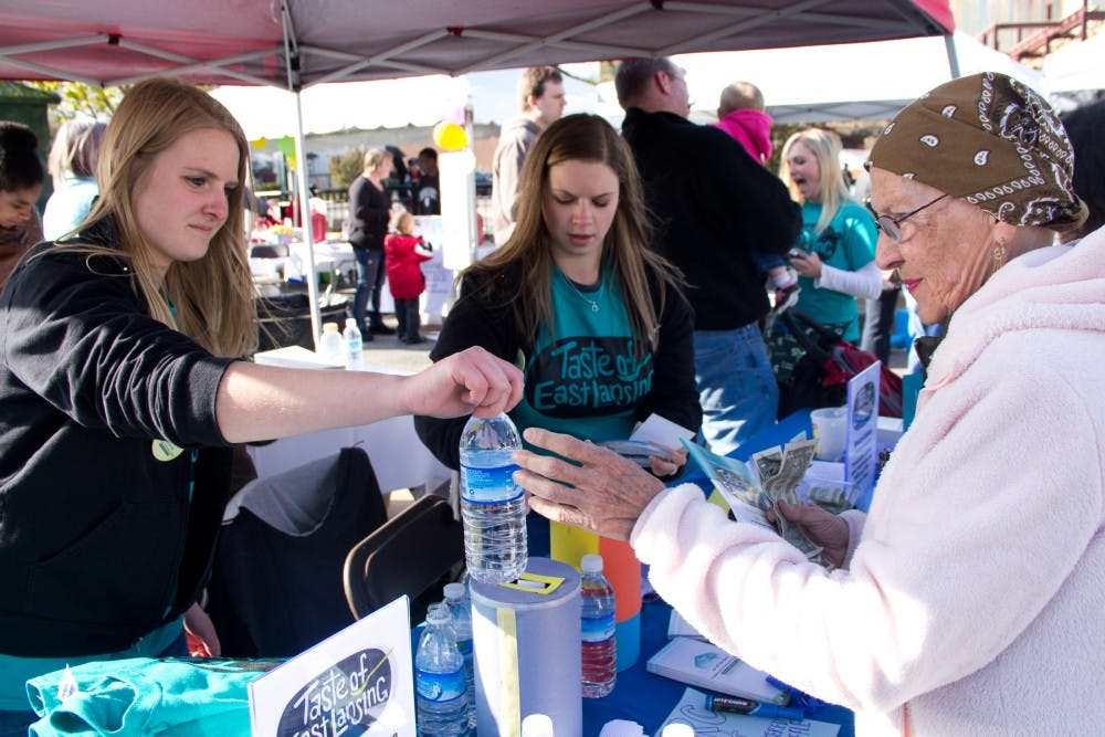 Communications senior Catie Musatics hands a water to East lansing resident, Carilyn Padgitt during the first-ever Taste of East Lansing event hosted by the city of East Lansing's Community Relations Coalition Saturday evening at Ann Street Plaza The event featured local food vendors, games, arts & crafts. Aaron Snyder/The State News 