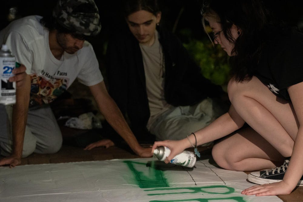 Graphic design freshman Grace Ferow sprays the Palestinian flag onto a banner at an anniversary memorial for Michigan State Humphrey fellow and Israeli bombing victim Tariq Thabet on Oct. 30, 2024.