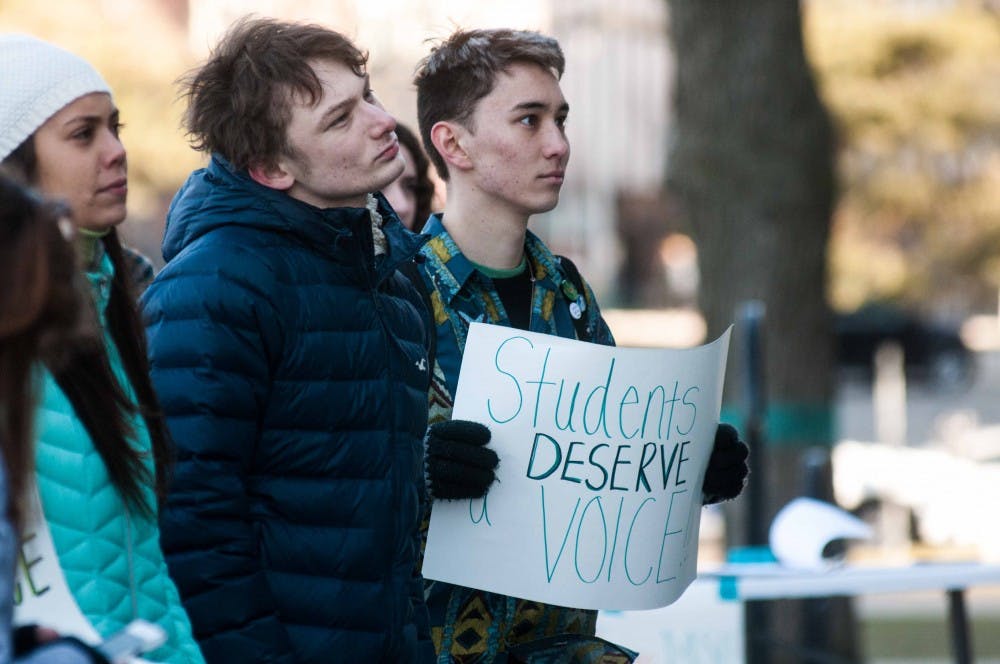 <p>Biochemistry and plant biology senior Traverse Cotrell, left, and environmental studies and sustainability sophomore, right, listen at the Reclaim MSU Rally at the Hannah Administration Building on March 23, 2018. (Annie Barker | State News)&nbsp;</p>