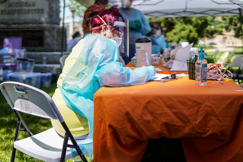 <p>A worker filling out paperwork in the COVID-19 testing station tent on the Capitol lawn during the Black Lives Matter protest at the Michigan State Capitol on June 29, 2020.</p>