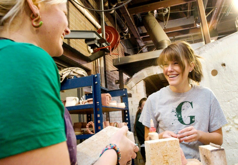 Art education seniors Jackie Alson, left, and Ashley Huiras share a laugh before they prepare pottery for the large gas kiln Tuesday afternoon at Kresge Art Center. Justin Wan/The State News