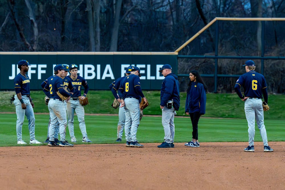 Michigan players talk on the field as umpires review a previous play during Michigan’s game against Michigan State at Jeff Ishbia Field at McLane Stadium in East Lansing, Mich., on Friday, April 10, 2026.