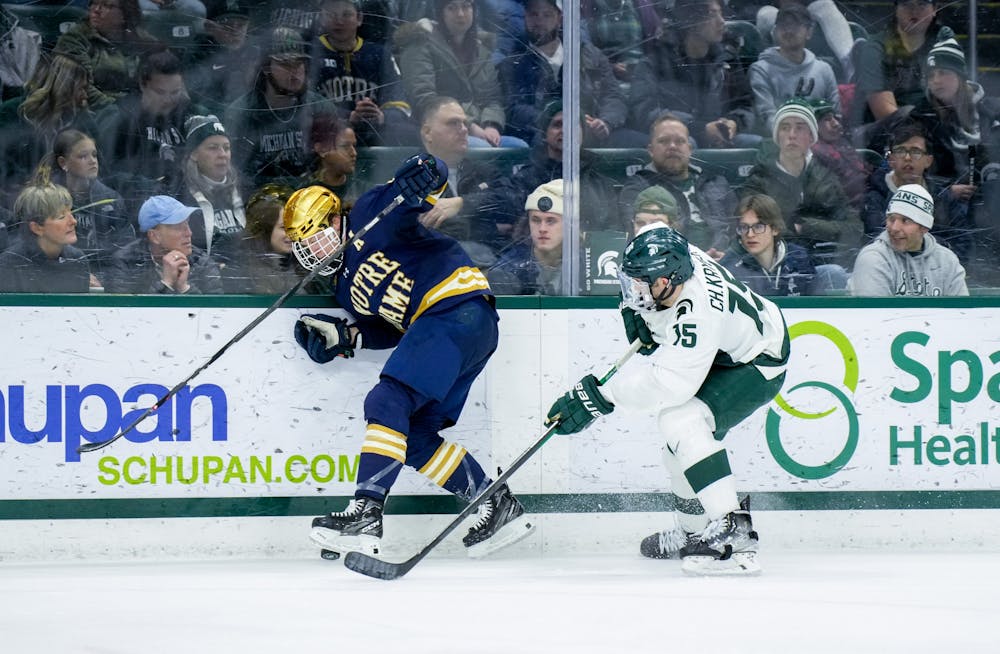 <p>Graduate student defender Christian Krygier (15) tries to get the puck from his opponent during a game against Notre Dame at Munn Ice Arena on Feb. 3, 2023. The Spartans defeated the Fighting Irish 3-0.</p>
