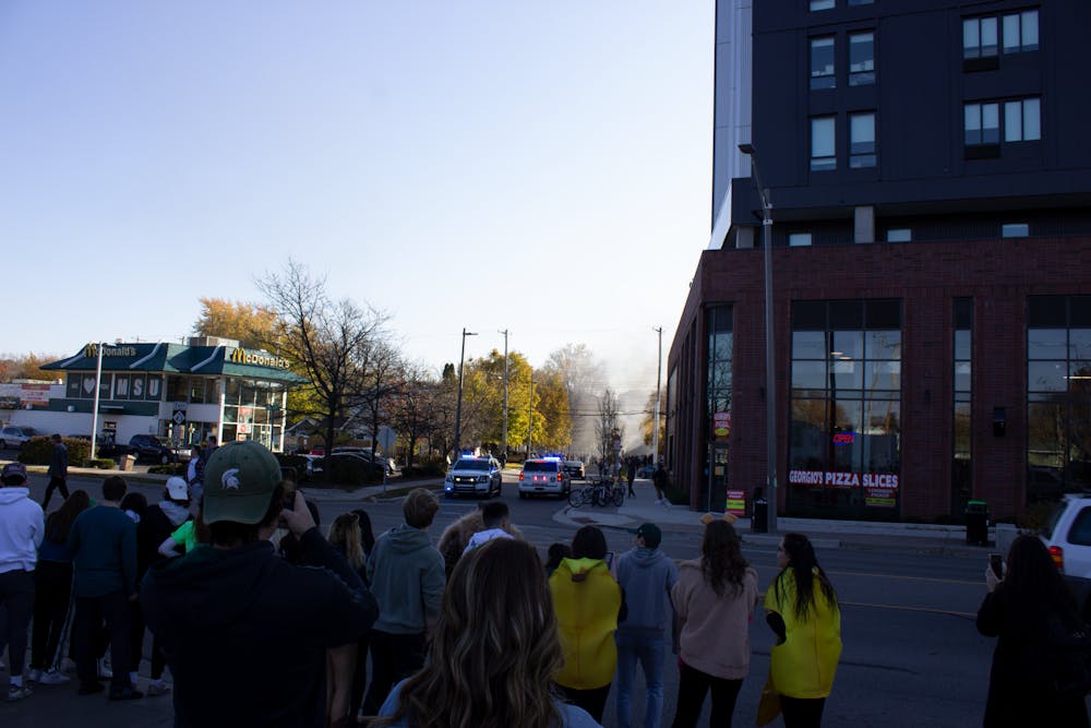 A group stands on Grand River Avenue watching smoke leave Cedar Village after Michigan State's win over the University of Michigan Oct. 31, 2020.