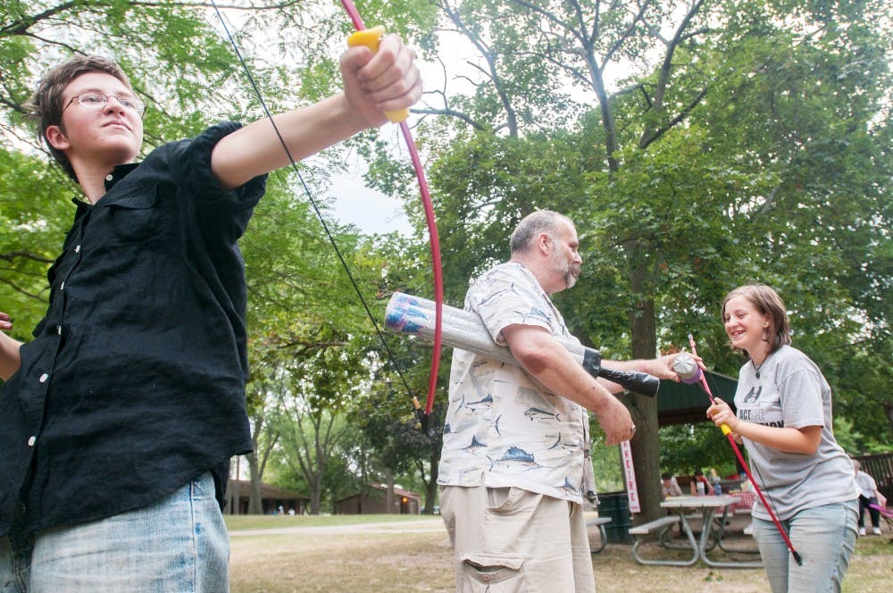 While Holt resident Zach Burton, left, fires a foam arrow, Lansing resident Jim Case and Holt resident Lexie Morgan, 15, chat during their family reunion in Patriarche Park, 1100 Alton St., on Sunday, July 22, 2012. The family were live action role playing, also known as LARPing. Julia Nagy/The State News