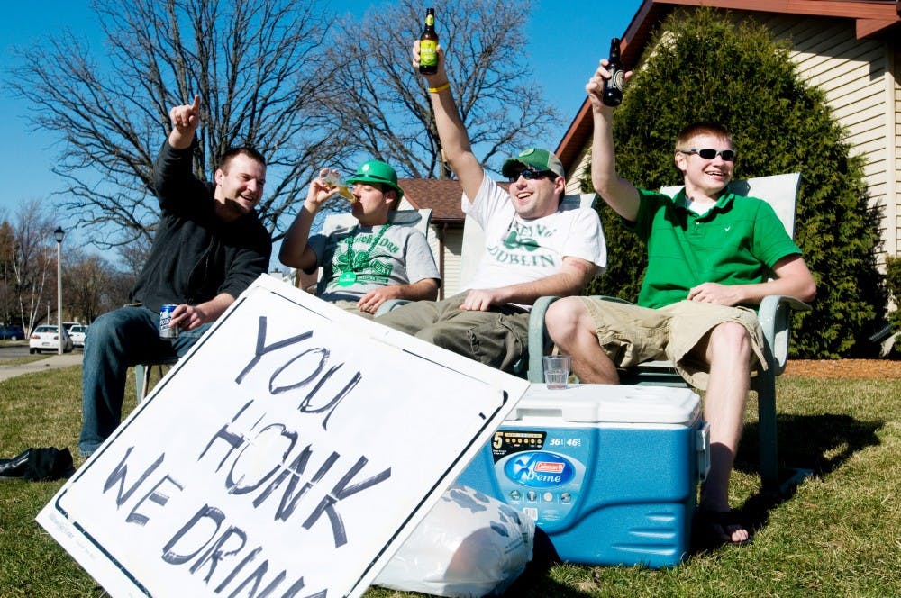 From left, Ferris State University student Matt Dobrowolski, interdisciplinary studies in social science and human resources and society senior Adam Carter, psychology senior Matt Carpenter and engineering senior Garrett Kerns raise their drinks after a car honked on Wednesday, St. Patrick's Day, at their duplex at 1309 Albert Ave. The group started at noon, and had a sign up that said "You Honk, We Drink." State News File Photo