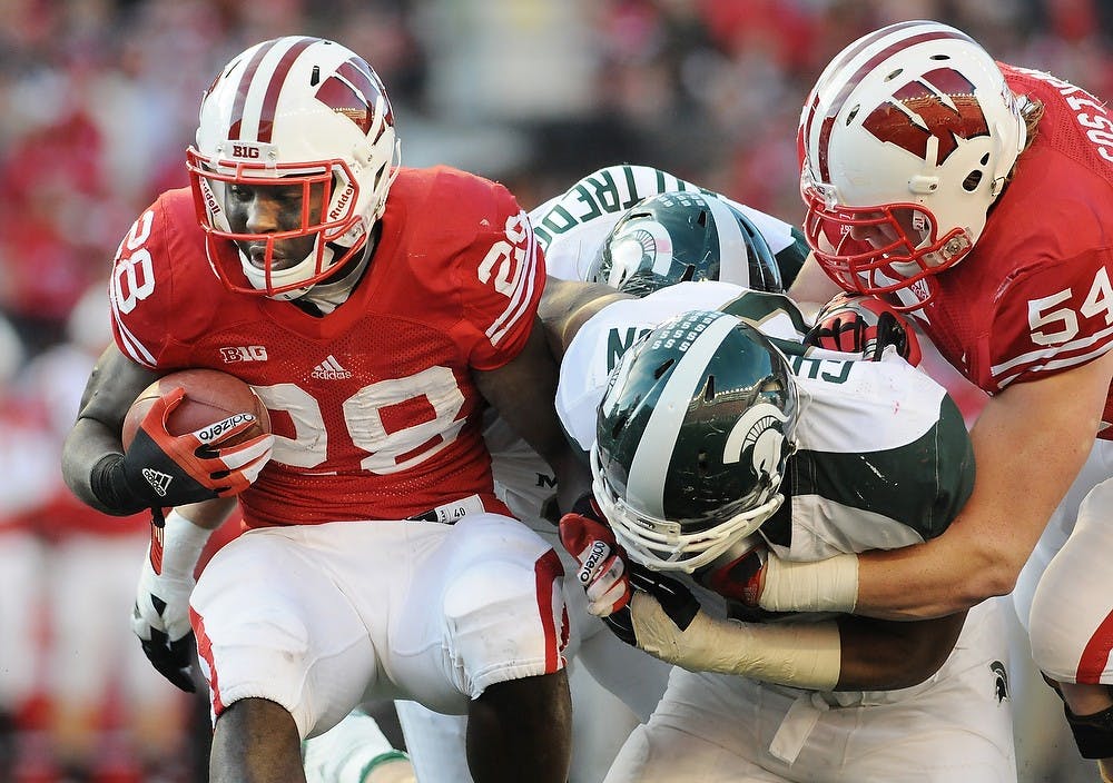 Junior defensive end William Gholston, center, tackles Wisconsin running back Montee Ball. Ball gained 46 yards for the Badgers, while MSU junior running back Le'Veon Bell had 77. Michigan State defeated Wisconsin in overtime, 16-13, on Saturday afternoon, Oct. 27, 2012, at Camp Randall Stadium in Madison, Wisc. Justin Wan/The State News