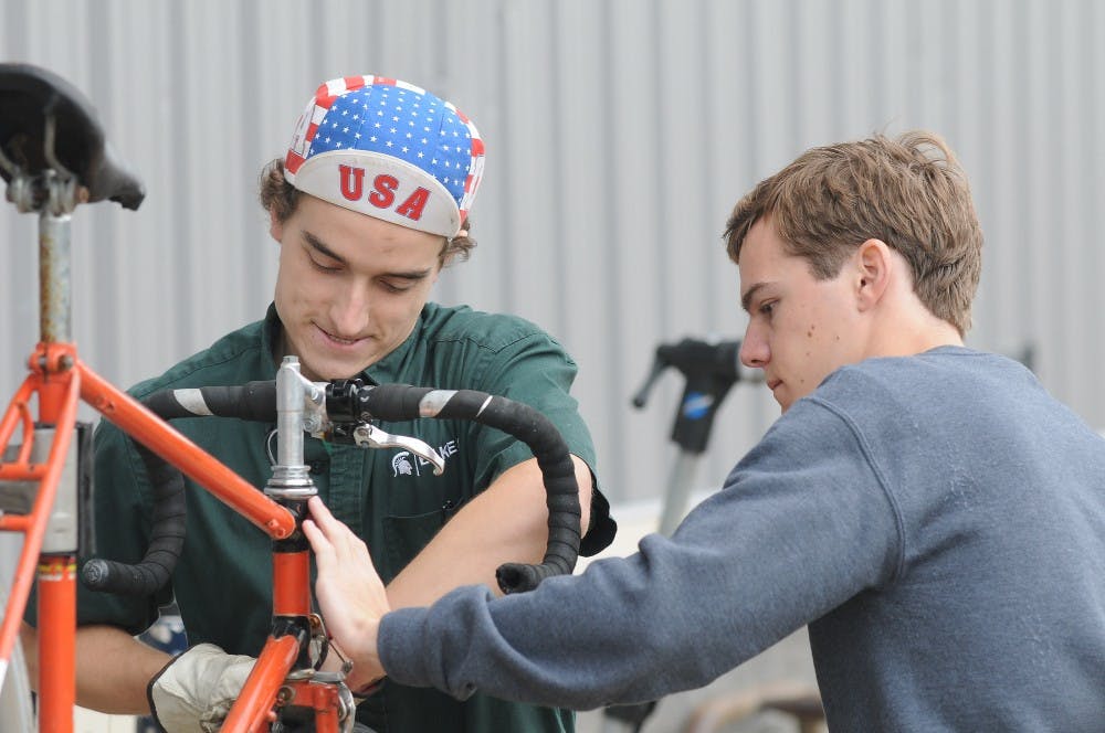 <p>Environmental studies and sustainability senior Michael Ewing (left) repairs a bike for lifelong education exchange student Guillaume Heral on Sept. 11, 2015 at the MSU Surplus Store. "I chose a bike for exercising," Heral said. "I want to ride a bike on campus, I think it's nicer than taking a bus on campus." Joshua Abraham/ The State News</p>