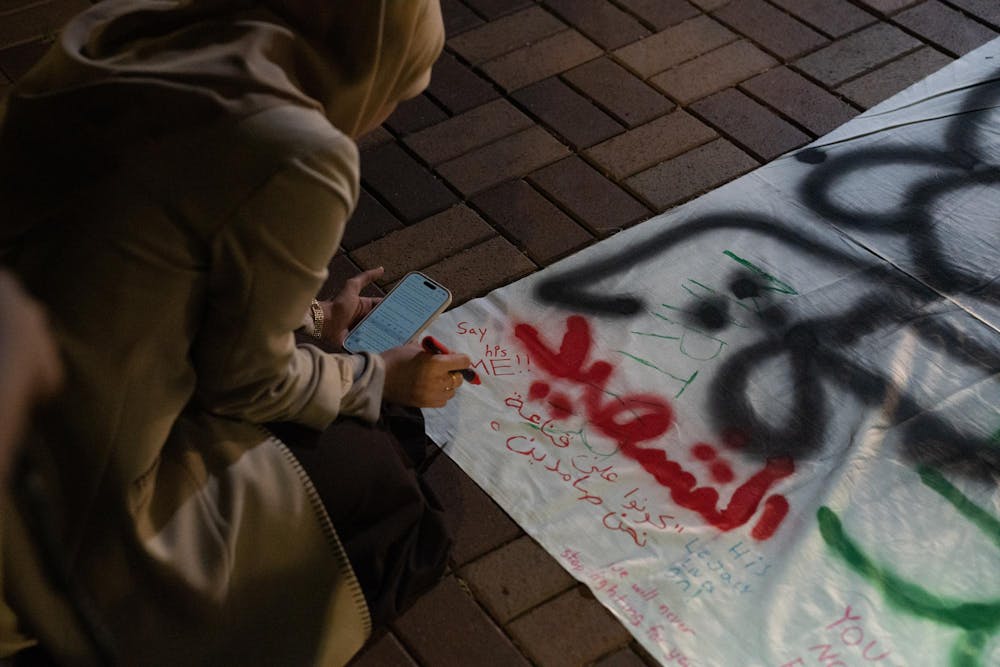 "Say his name," writes human biology junior Aesha Zakaria onto a banner at an anniversary memorial for Michigan State Humphrey fellow and Israeli bombing victim Tariq Thabet on Oct. 30, 2024. Zakaria was in contact with Thabet shortly before his death last year.