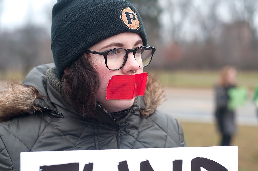 <p>Lansing resident Liz McDaniel covers her mouth with tape Dec. 13, 2014 during a protest against commencement speaker, George Will outside of Breslin Center. McDaniel said that the tape symbolized that this was a peaceful protest. Jessalyn Tamez/The State News </p>