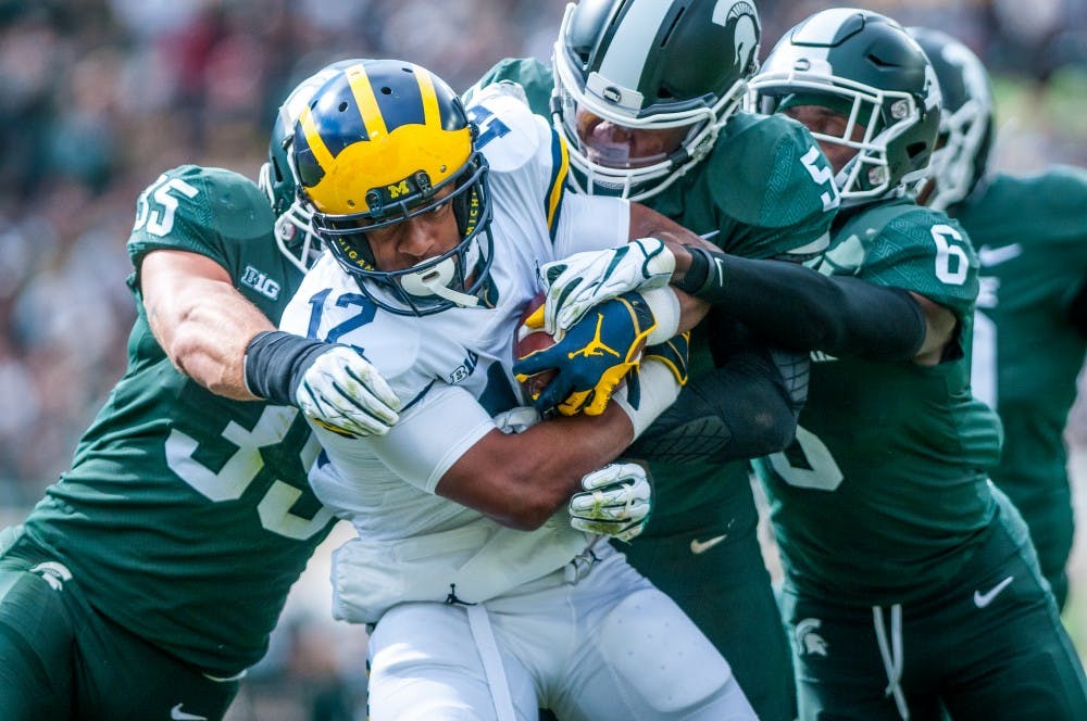 Michigan running back Chris Evans (12) is tackled by multiple Spartans during the game against Michigan on Oct. 20, 2018 at Spartan Stadium. The game was scoreless at the rain delay in the first quarter.