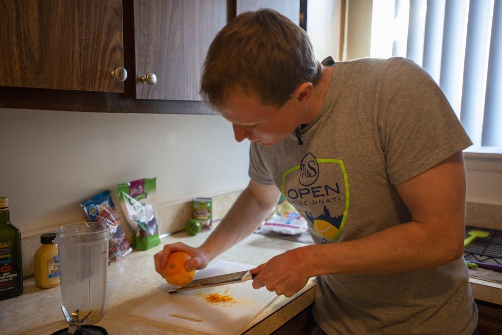 <p>MSU evolutionary biology and genetics senior Nick Stants zests an orange in his apartment kitchen. On April 8, Stants published a salads cookbook for young adults.</p>