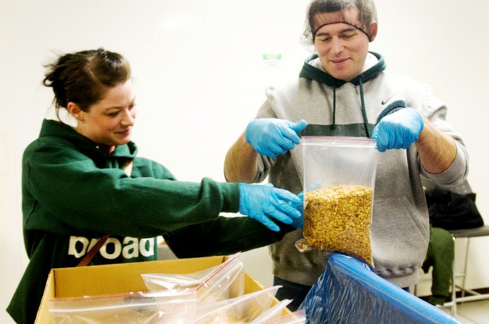 Marketing graduate student Alicia Luzkow holds a bag of cereal as business graduate student Jeff Brown seals it shut Friday at the Mid-Michigan Food Bank, 2116 Mint Road, Lansing. The MBA Association and the College of Osteopathic Medicine student government worked together at the food bank packing boxes and bagging cereal to give back to the community as well as foster a stronger relationship between the graduate student groups. Jaclyn McNeal/The State News