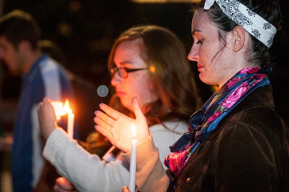 <p>Business hospitality senior Lydia Olson holds a lit candle to memorialize those lost in 9/11 on Sept. 11, 2014, at the Rock on Farm Lane. Raymond Williams/The State News</p>