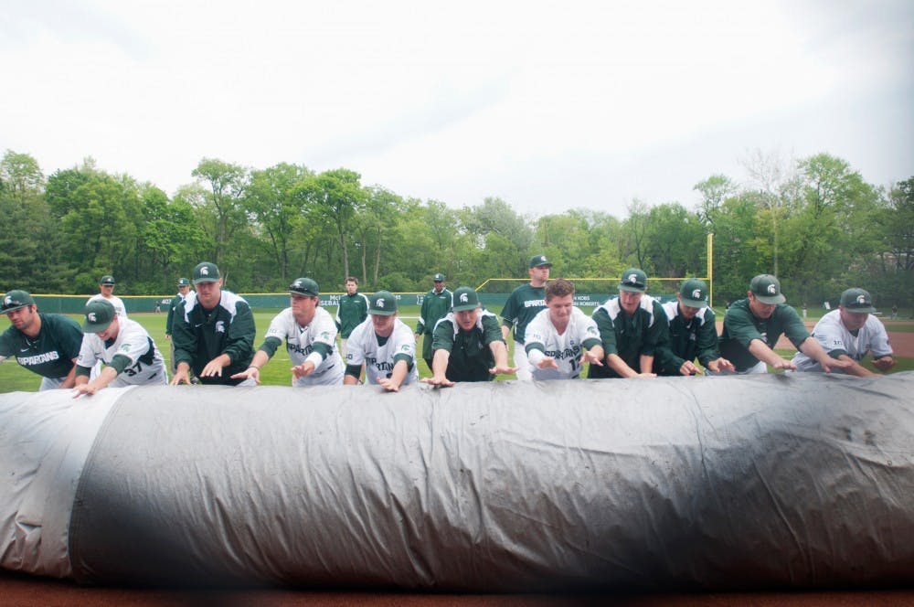 Michigan State players and coaches role up a tarp that protected the field from the rain just before Michigan State faced Iowa Saturday afternoon at McLane Baseball Stadium at Old College Field. The Spartans lost to the Hawkeyes 2-1.Samantha Radecki/The State News