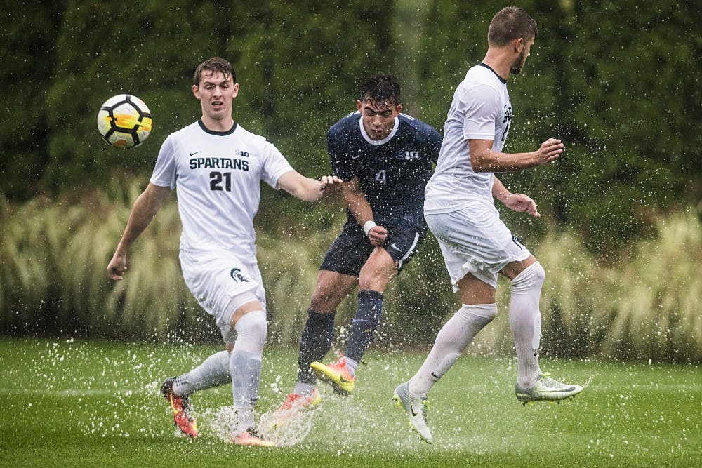 Sophomore forward Michael Beckett (21) and Penn State defense Brennan Ireland (4) attempt to head the ball during the game against Penn State on Oct. 14, 2017 at DeMartin Stadium. The Spartans defeated the Nittany Lions in the pouring rain, 1-0.