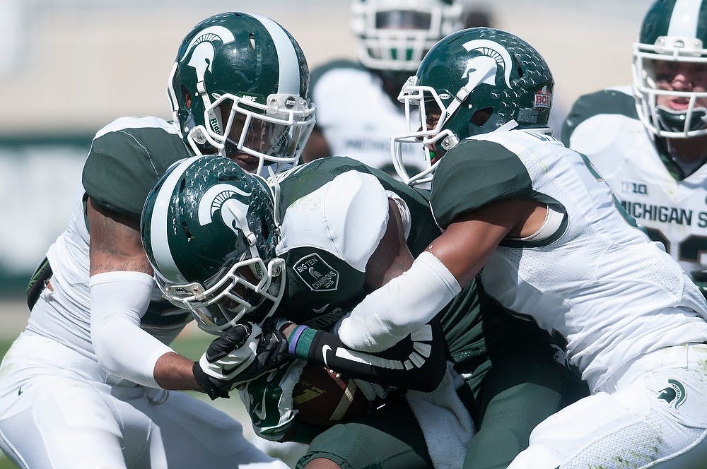 <p>Senior safety Kurtis Drummond, left, and sophomore cornerback Darian Hicks tackle senior wide receiver Tony Lippett on April 26, 2014, during the Spring Green and White game at Spartan Stadium. The White team won, 20-13. Julia Nagy/The State News</p>