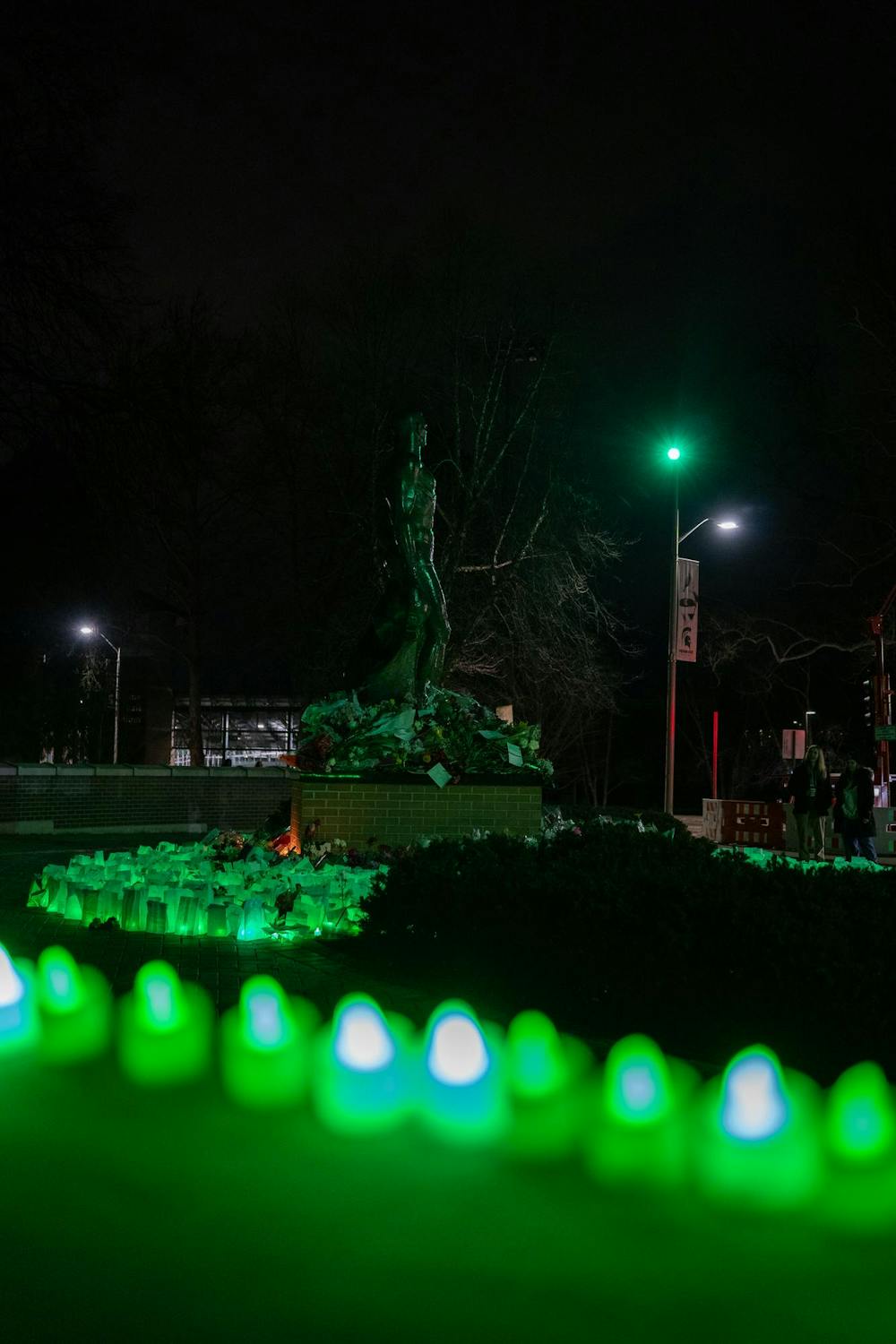 <p>Green-lit luminaries, flowers and supportive messages surround the Spartan Statue on Feb. 13, 2024. One year after the Michigan State University campus shooting, a remembrance ceremony was held to remember and reflect on the tragedy.</p>