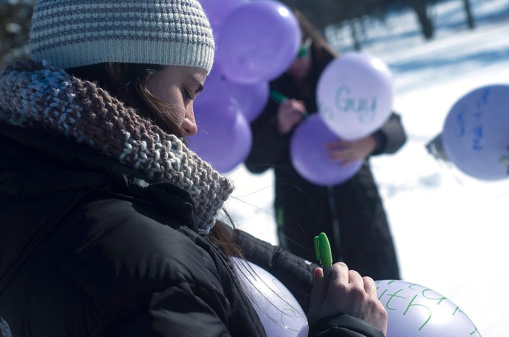 <p>Senior supply chain management major Lauren Murphy of Spartans Fighting for Cancer Club writes "Spartans with Cancer" on a balloon as a testimony to those students battling cancer during their Relay for Life balloon release Feb. 5, 2015, at the rock. Camille Douglas/The State News</p>