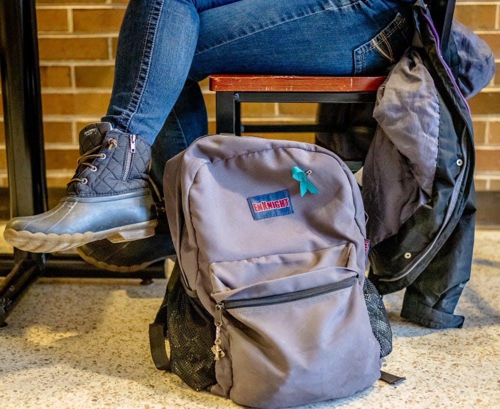 <p>Communications junior Maddie Jones rests her backpack, pinned with her teal ribbon, next to her while she studies on Jan. 22, 2019 at the Communication Arts and Sciences Building.</p>