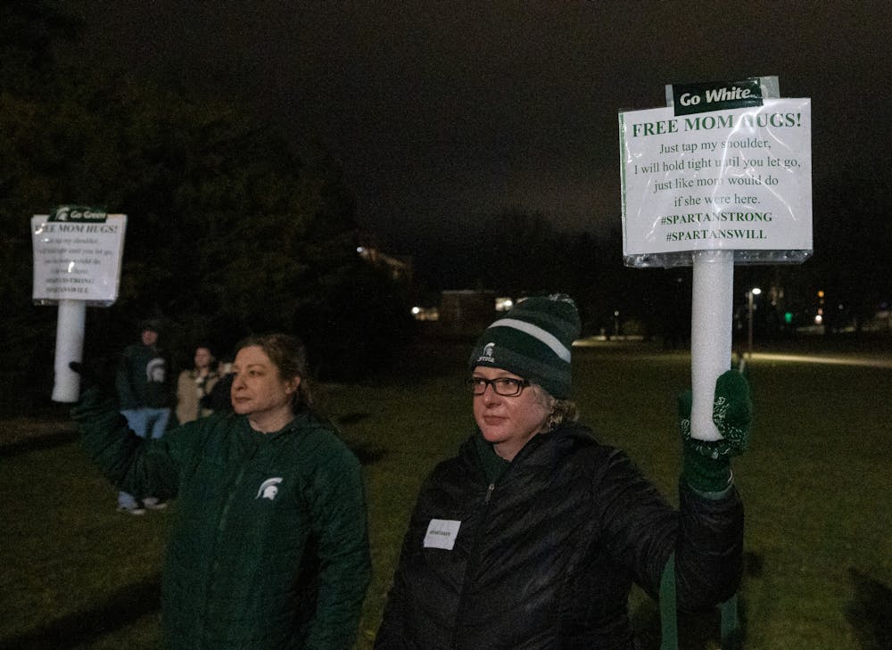 East Lansing mom’s hold signs that read, “FREE MOM HUGS!” at the Rock on Farm Lane for a vigil that took place on campus on Feb. 15, 2023. Michigan representatives, MSU President Theresa Woodruff and MSU ASMSU President Jo Kovach were some of the speakers that expressed their sympathy for the victims,  injured and MSU community. 