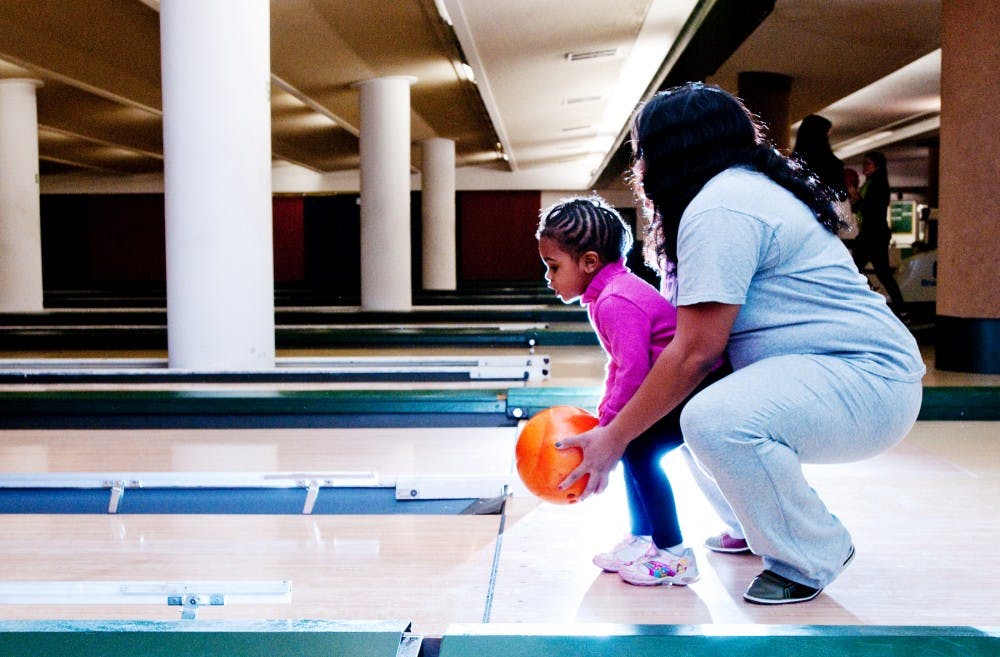 Social work senior Natalie Kyles helps her daughter, Kadence Carr, 3, bowl during an event put on by the School of Social Work for foster care system alumni on Tuesday night at the bowling alley in the Union. Students were given a free opportunity to bowl as well as "finals week survival kits" to help with the added stress next week as finals approach. Josh Radtke/The State News