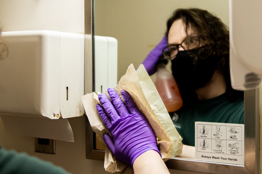 Skylar Ward cleans an exam room's bathroom mirror in Olin Health Center on Feb. 3, 2021.