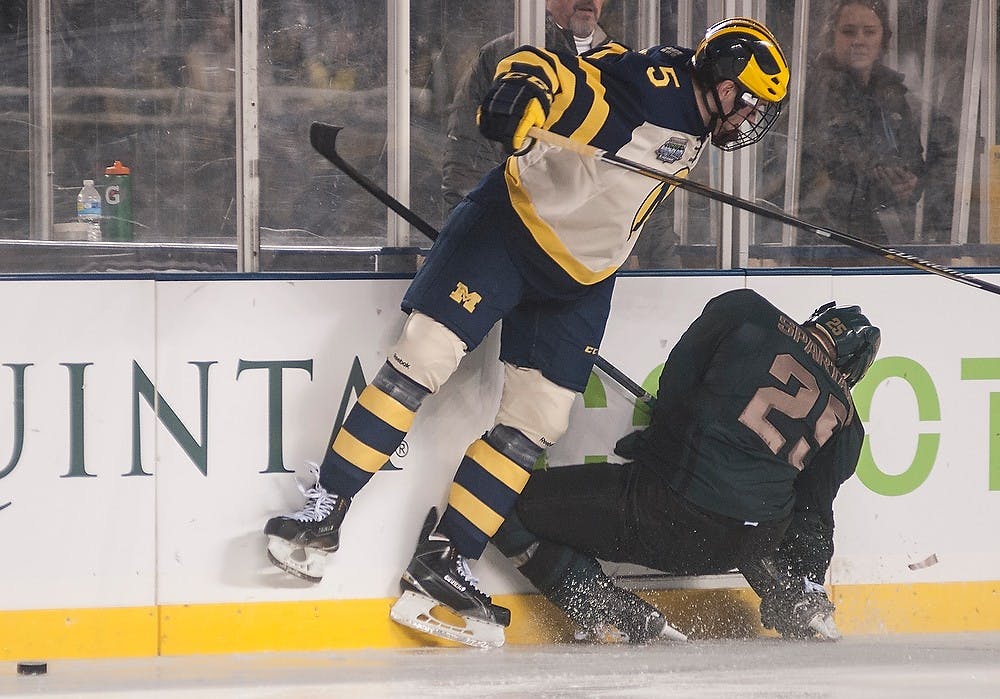<p>Senior forward Brent Darnell falls to Michigan defenseman Michael Downing Feb. 7, 2015, during the game against Michigan at Soldier Field in Chicago, Illinois.  The Spartans were defeated by the Wolverines, 4-1, during the Coyote Logistics Hockey City Classic. Alice Kole/The State News</p>